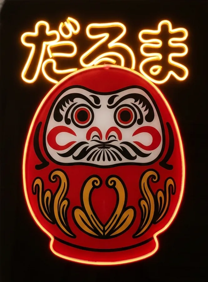 Cuadro Daruma: figura roja de la buena suerte con caligrafía japonesa perfilada en Neon Flex ámbar sobre panel negro.